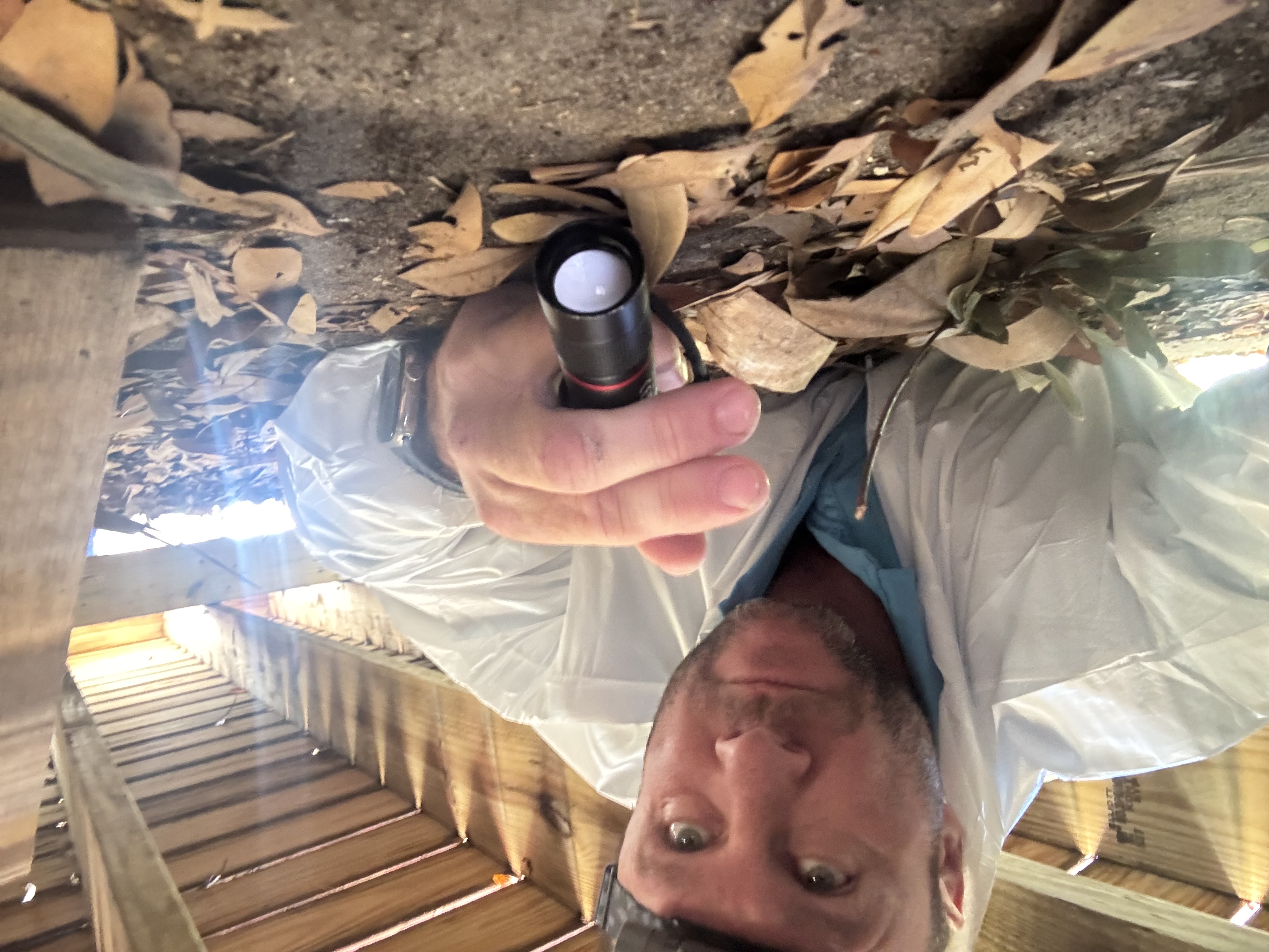 Johnny Thompson inspecting a crawl space with flashlight and protective gear